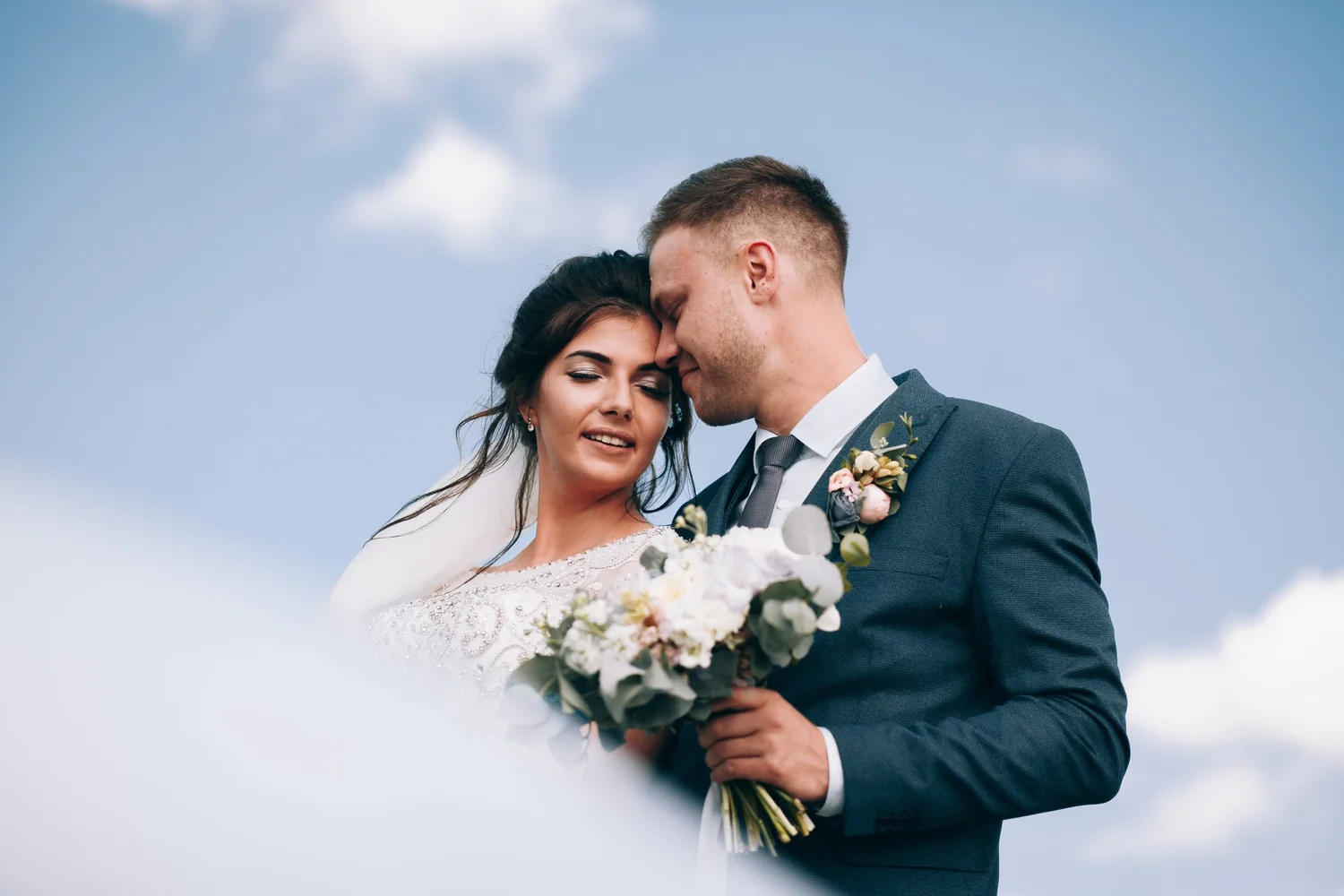 Bride and groom embracing against a bright Texas sky